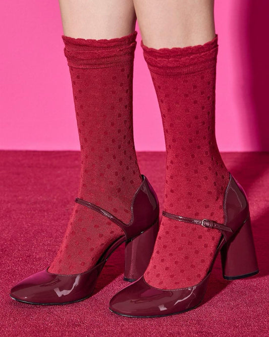 Red high-heeled shoes with matching socks with polka dot pattern and scalloped frill cuff on a pink background