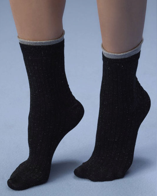 A pair of black ribbed crew socks with a gray elastic cuff, shown on a person's feet against a light blue-gray studio background.
