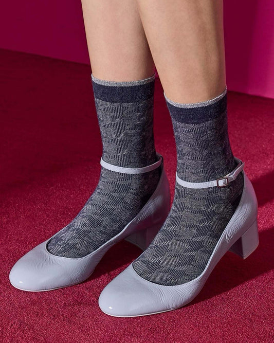 Grey and navy houdstooth patterned socks with pale clue shoes on a red background