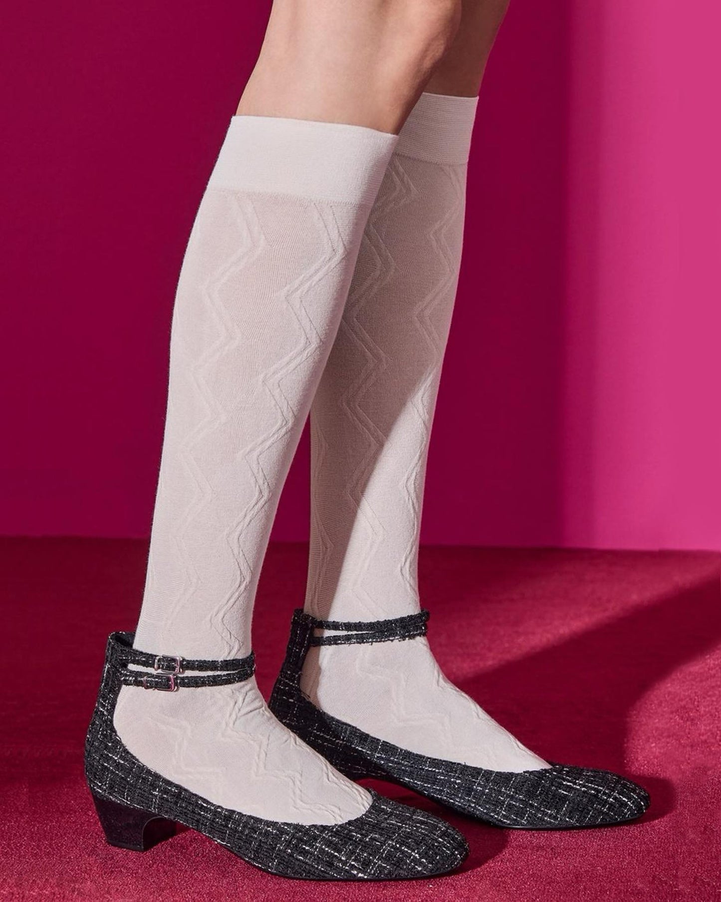 White knee-high socks with a zig-zag pattern worn with black check patterned shoes on a red background