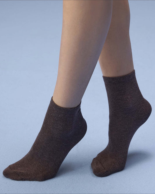 A pair of dark brown ankle socks worn on a person's feet, shown against a solid light blue-gray studio background.