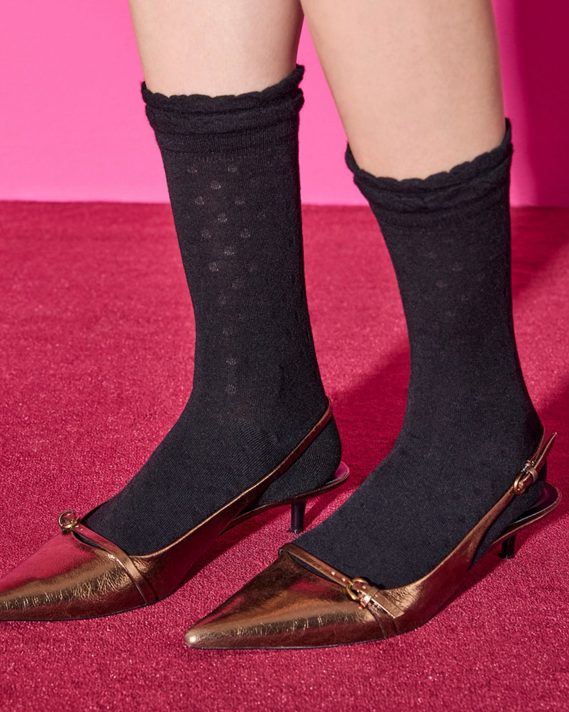 Black polka dot socks with filly scalloped cuff, worn with bronze kitten-heeled shoes on a pink background