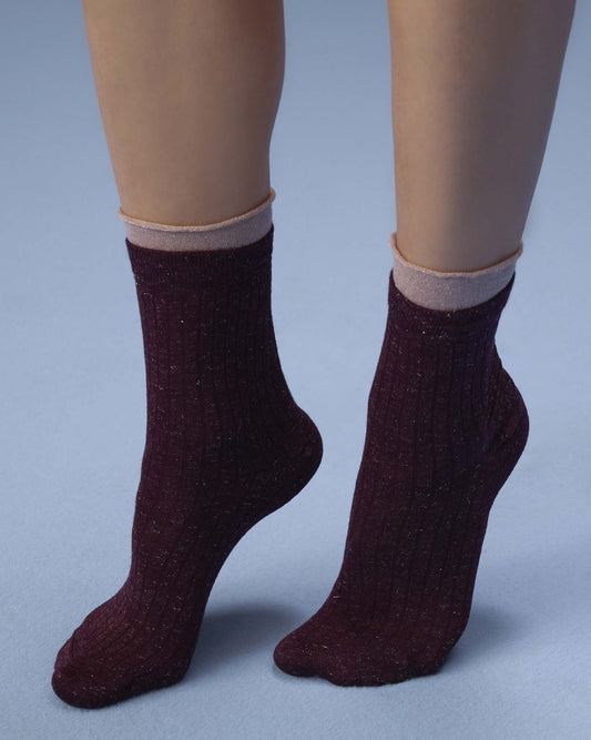 A pair of ribbed ankle socks in a deep burgundy color with a subtle glitter texture, shown on a mannequin's feet against a light blue-gray background.