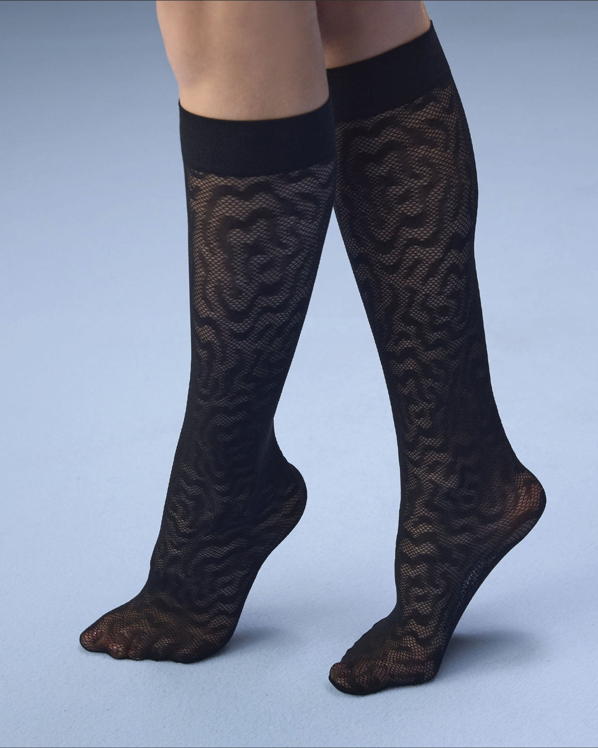 Black knee-high lace socks with a wavy pattern, shown on a model's legs against a light blue studio background.