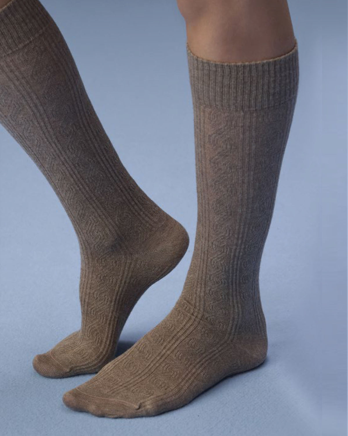 A pair of knee-high ribbed socks with a subtle cable-knit pattern, shown worn on a person's legs against a solid blue-gray studio background.