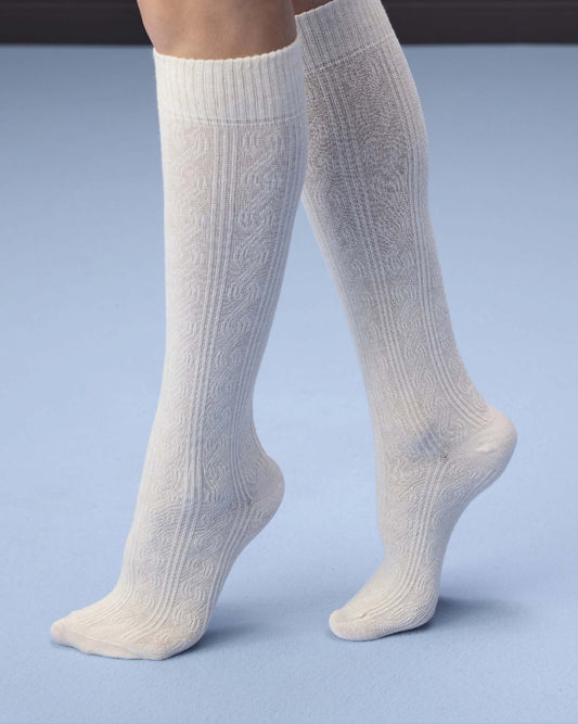 A pair of off-white cable-knit knee-high socks worn on legs, shown against a light blue studio background.